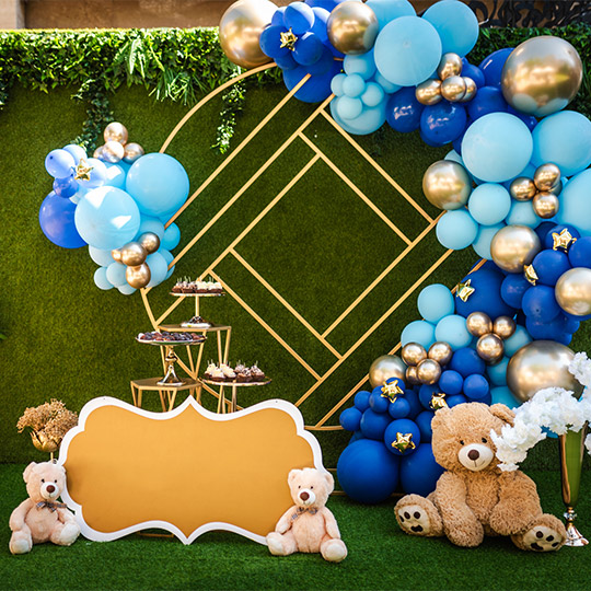 Decoration for a children's party with brown teddy bears, blue and gold balloons and green grass